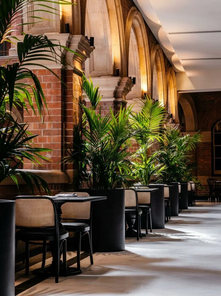 Restaurante de alta gama con arcos de ladrillo, jardineras monumentales y sillas negras con respaldo de rejilla